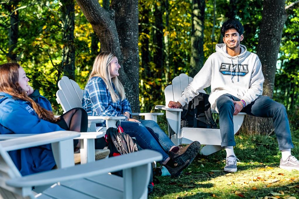 三个学生坐在树林前的阿迪朗达克椅上