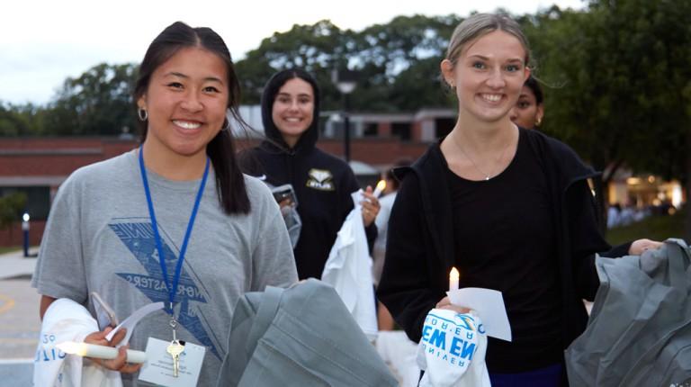 Three new undergrad students holding candles and Nor'easter t-shirts during First Night