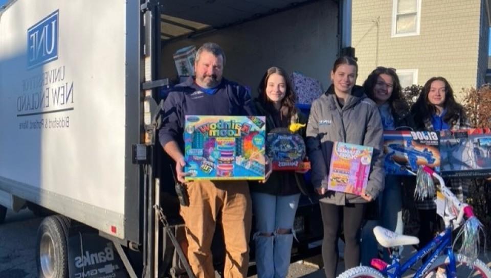 学生 和 volunteers pose in front of a box truck holding toys 和 gifts for Seeds of Hope