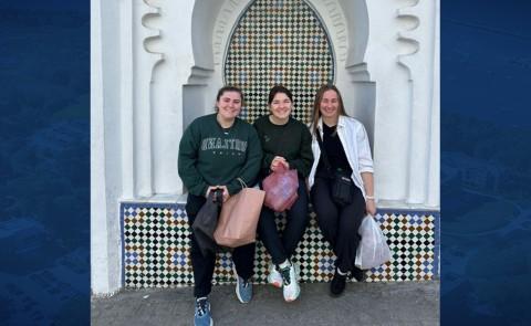三名女学生在摩洛哥建筑前摆姿势. 照片设置在蓝色背景下.
